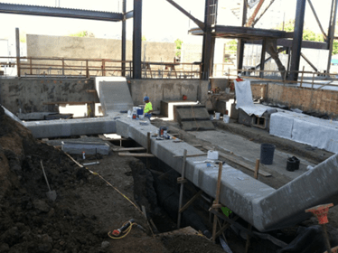 Construction site with a partially completed concrete structure surrounded by earth and building materials, indicating ongoing development work.