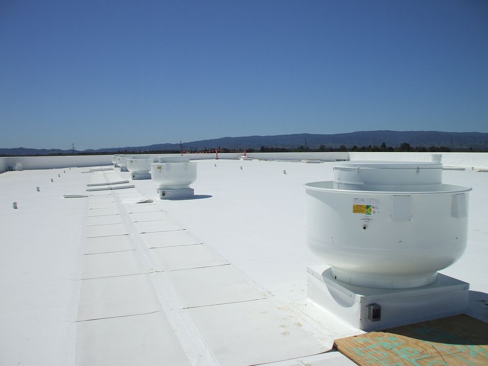 HVAC units line a flat commercial rooftop under a clear blue sky, with distant mountains in the background, highlighting a focus on building ventilation systems.
